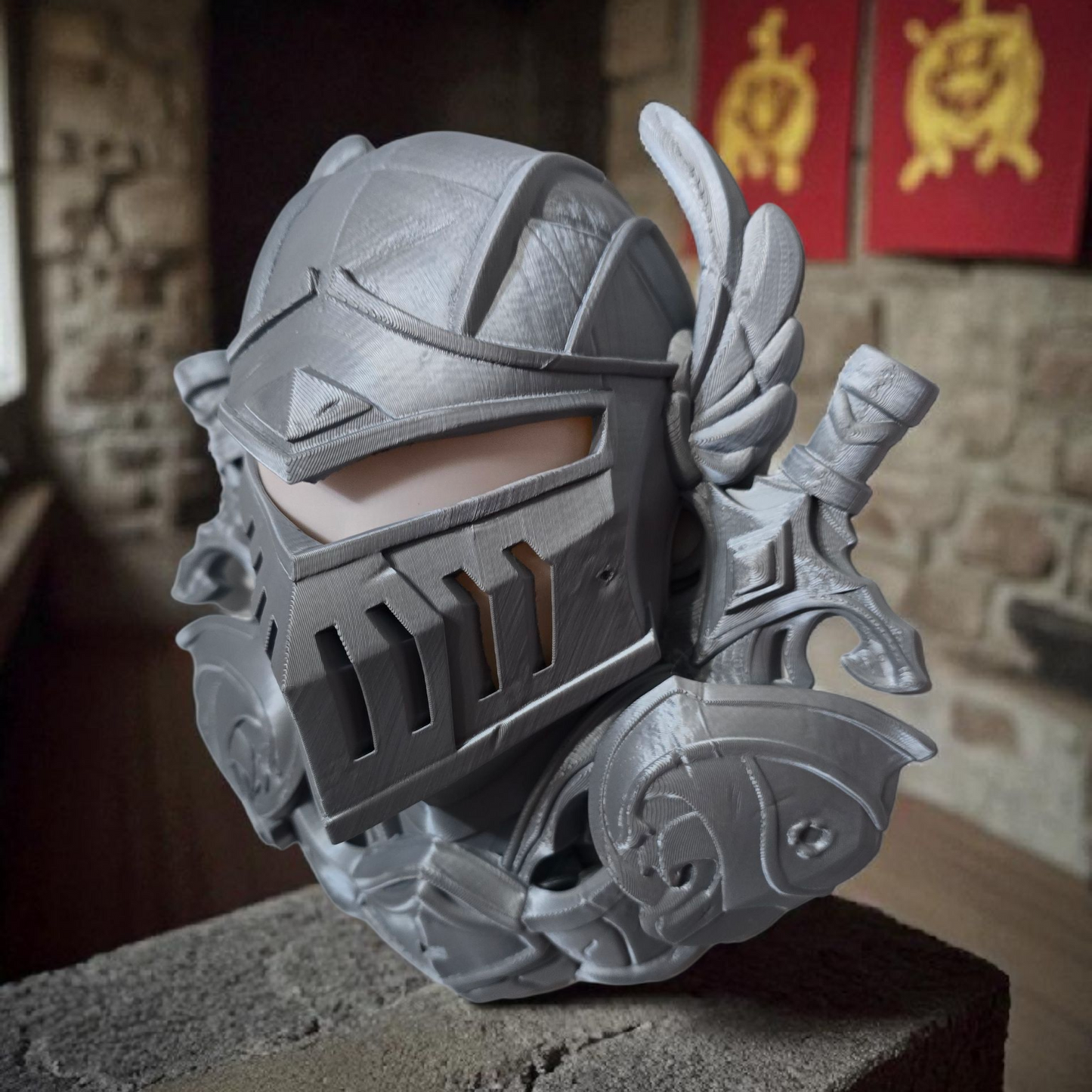 Decorative helmet with wings on a stone surface, with a stone wall and red banners in the background.