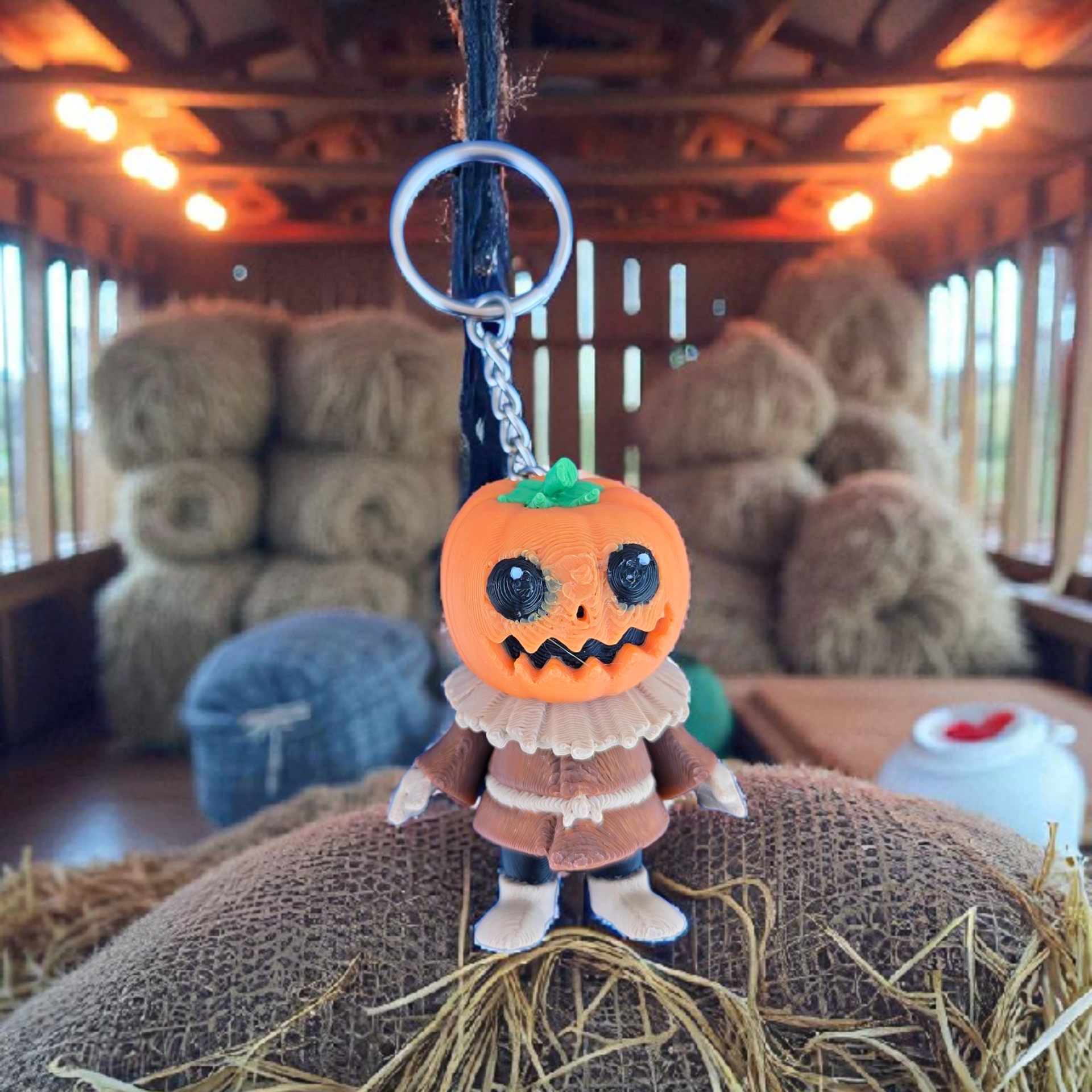 Pumpkin-shaped keychain with a character design hanging on a string in a barn setting.